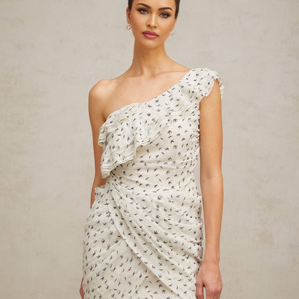 Woman wearing short white dress with ruffles and printed pattern standing against plain background