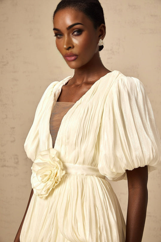 Woman wearing sleeveless beige mini dress with pleated skirt and floral applique details