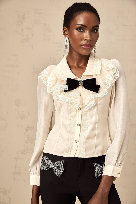 Woman wearing white buttonup shirt with lace trim and bow detail at neckline