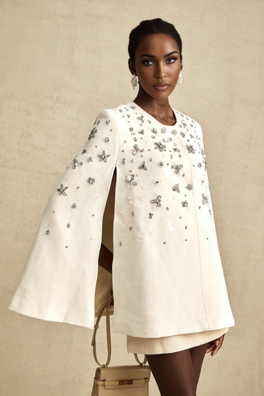 Woman wearing white cape jacket with ornate embellishments and flowing design