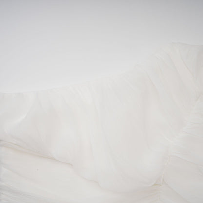 Woman wearing white creased fabric top and matching trousers standing against plain background