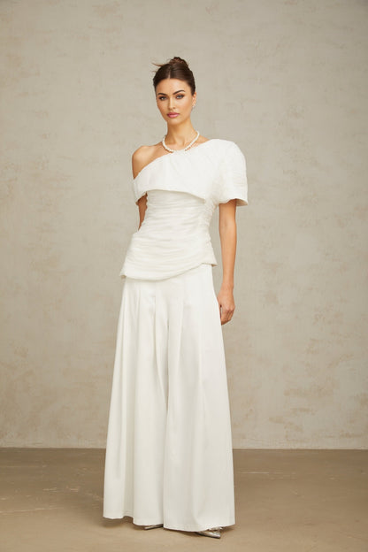Woman wearing white creased fabric top and matching trousers standing in relaxed pose