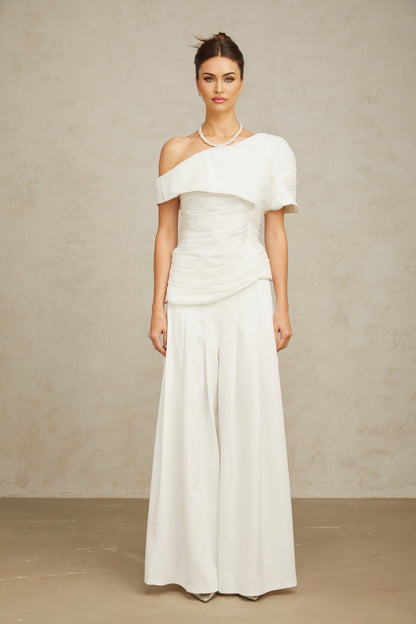Woman wearing white creased top and matching trousers set standing in relaxed pose