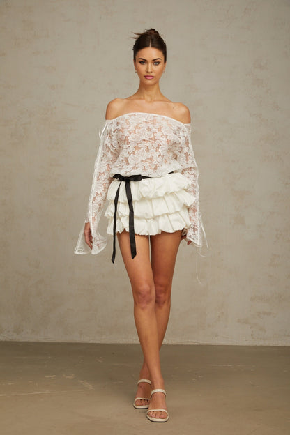 Woman wearing white floral lace matching crop top and skirt set against plain background