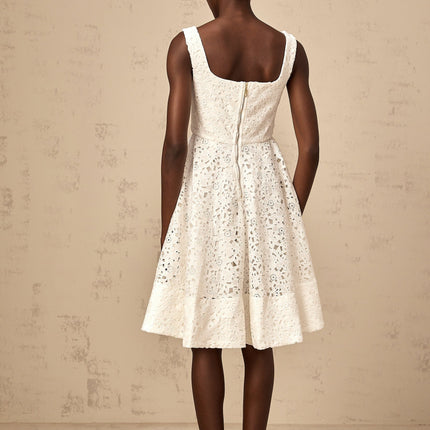Woman wearing white floral lace midi dress with fitted bodice and flowing skirt standing against plain background