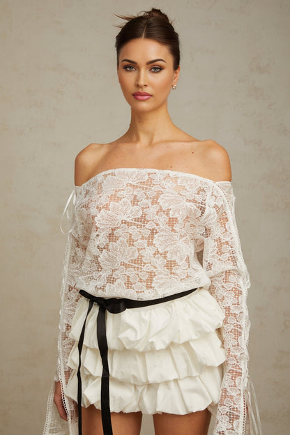 Woman wearing white floral lace top and matching skirt set standing against plain background