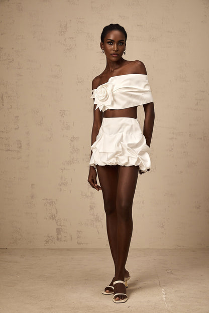 Woman wearing white floral patterned matching set with pleated top and skirt standing against neutral background
