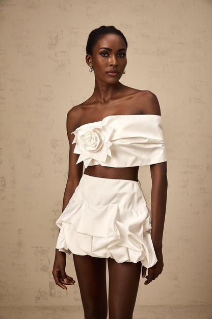 Woman wearing white floral pleated top and matching skirt set by Honorine standing against plain background