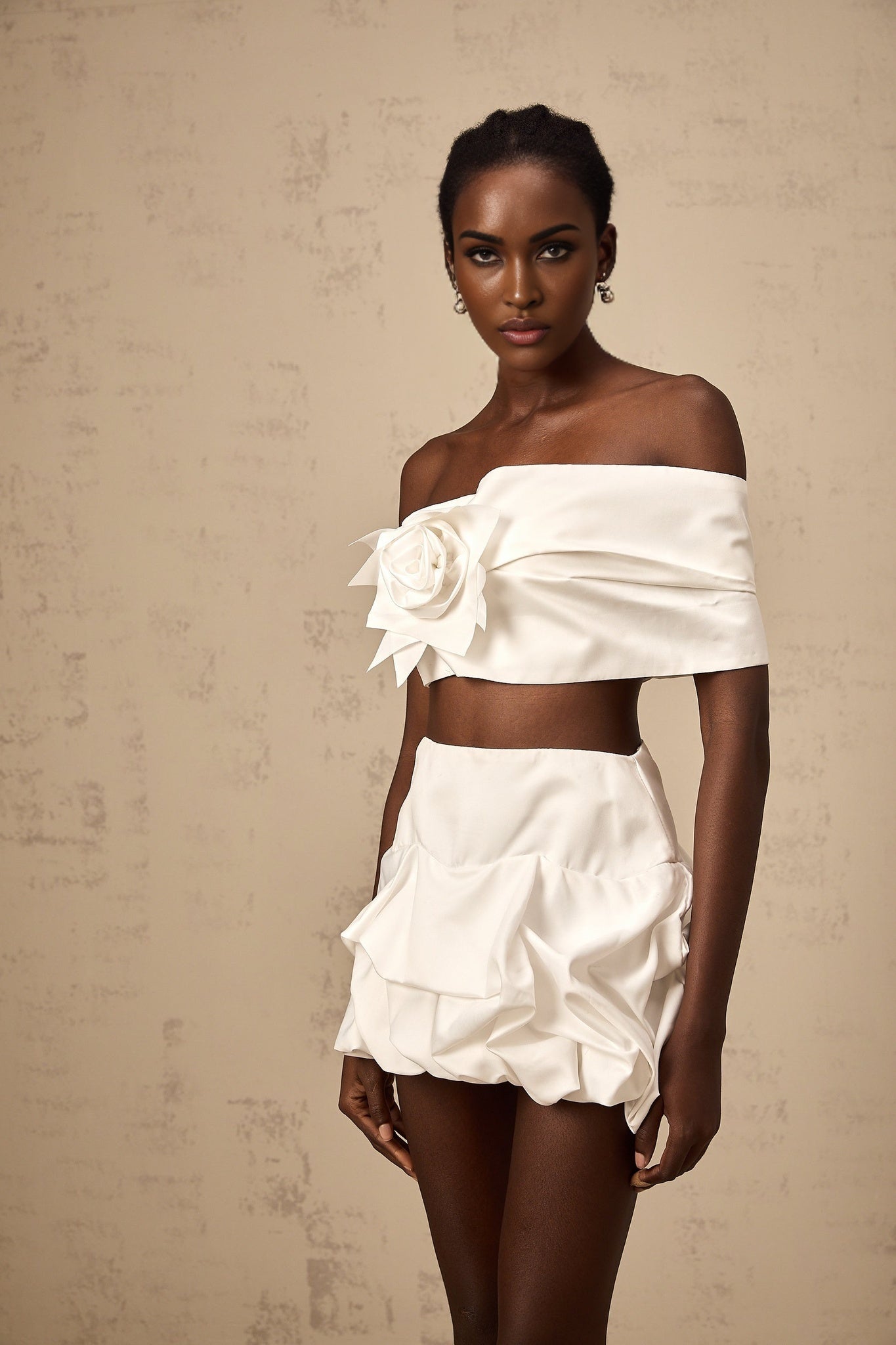 Woman wearing white floral printed matching top and skirt set with pleated details standing against neutral background