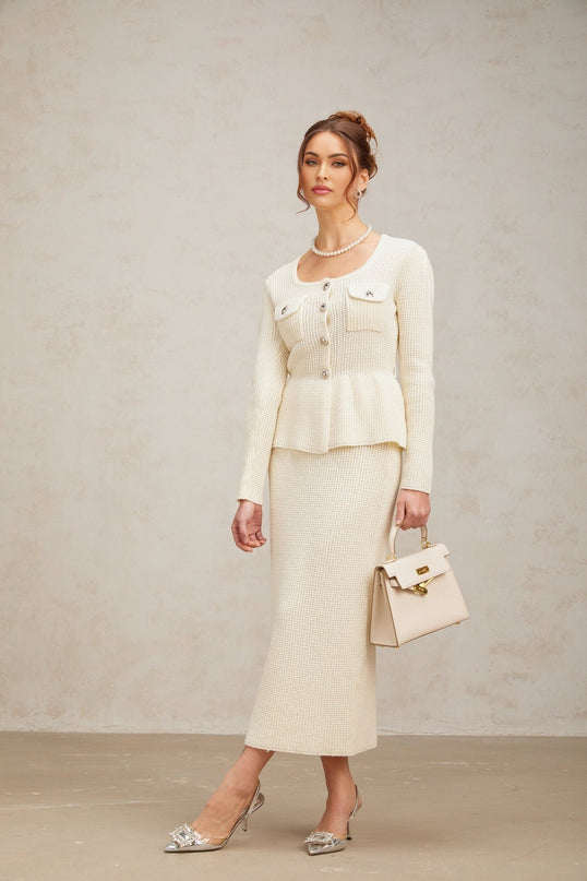 Woman wearing white knitted sleeveless top and matching midi skirt set standing against plain background