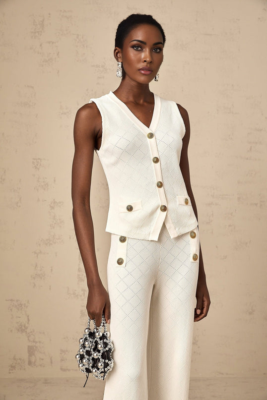 Woman wearing white knitted top and matching trousers set standing against plain background