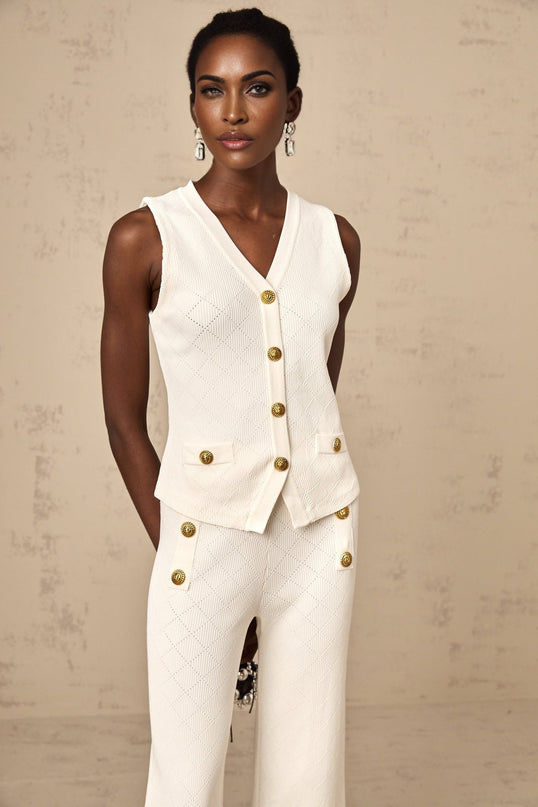 Woman wearing white knitted top and matching trousers standing against plain background