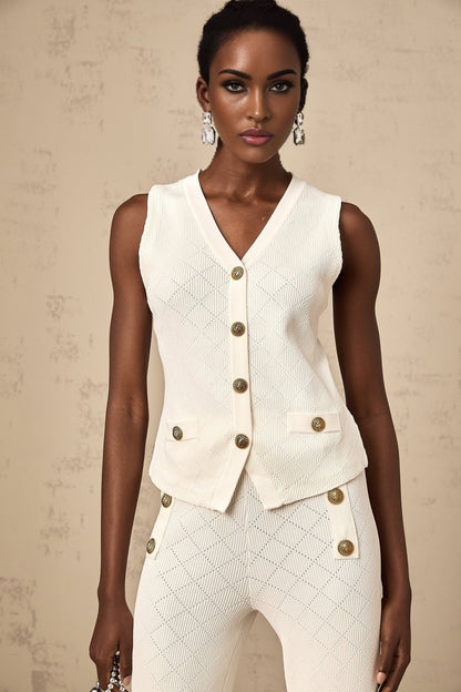 Woman wearing white knitted top and matching trousers standing against plain background