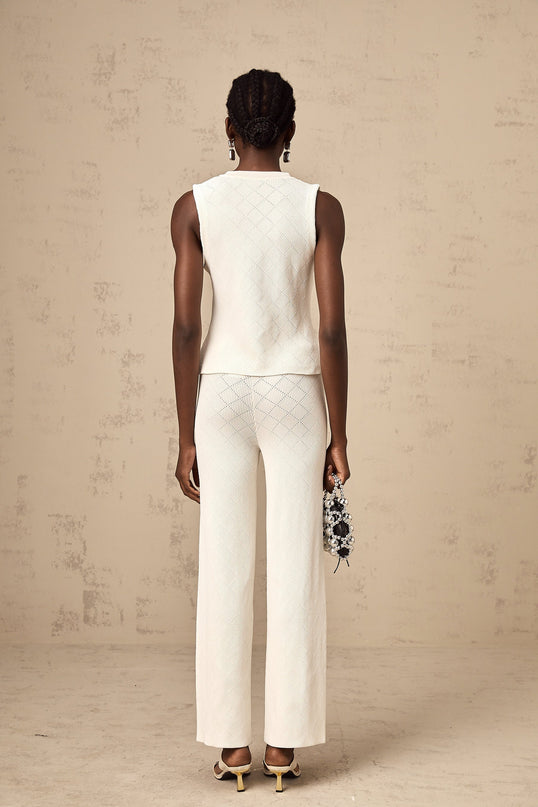 Woman wearing white knitted top and matching trousers standing in relaxed pose against plain background