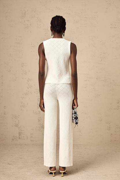 Woman wearing white knitted top and matching trousers standing in relaxed pose against plain background