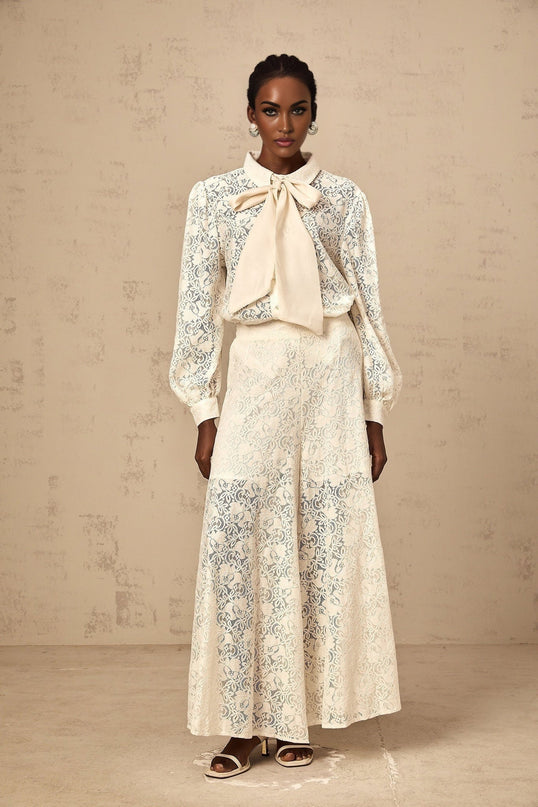 Woman wearing white lace shirt and matching trousers standing against plain background