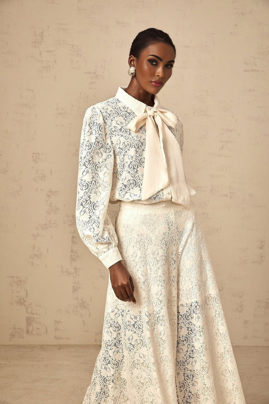 Woman wearing white lace shirt and matching trousers standing in a neutral background