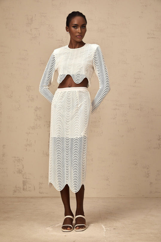 Woman wearing white matching set with wavy woven texture top and skirt standing against plain background