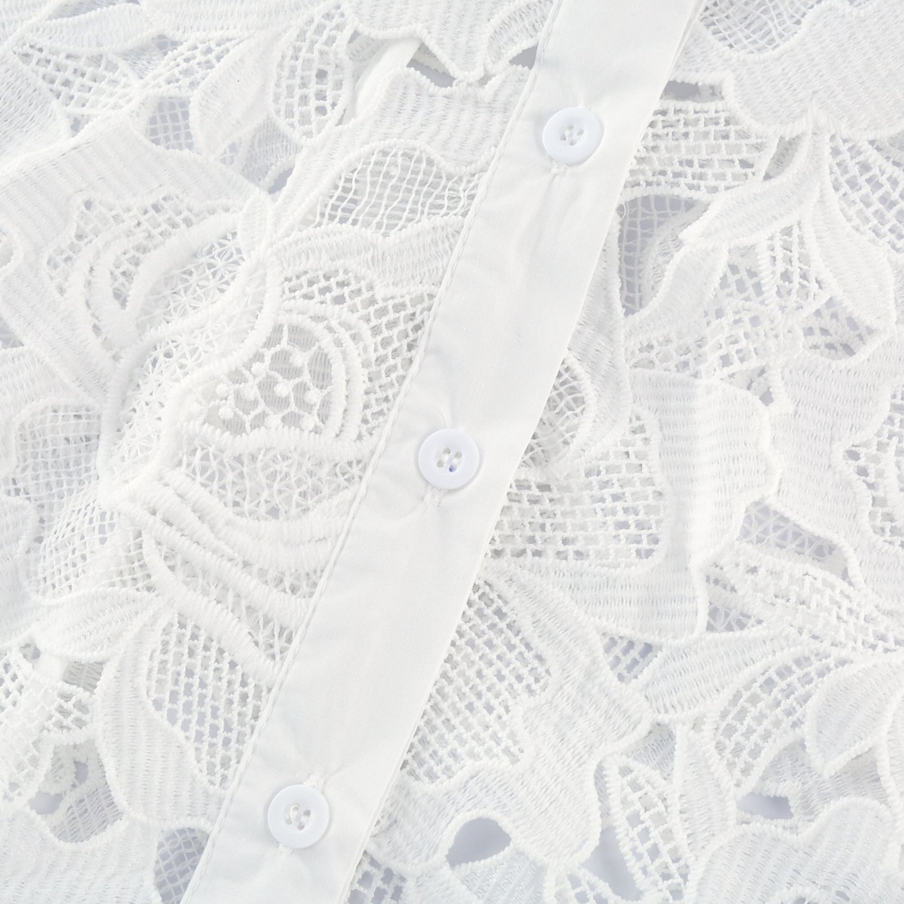 Woman wearing white midi dress with floral embroidery details standing against plain background