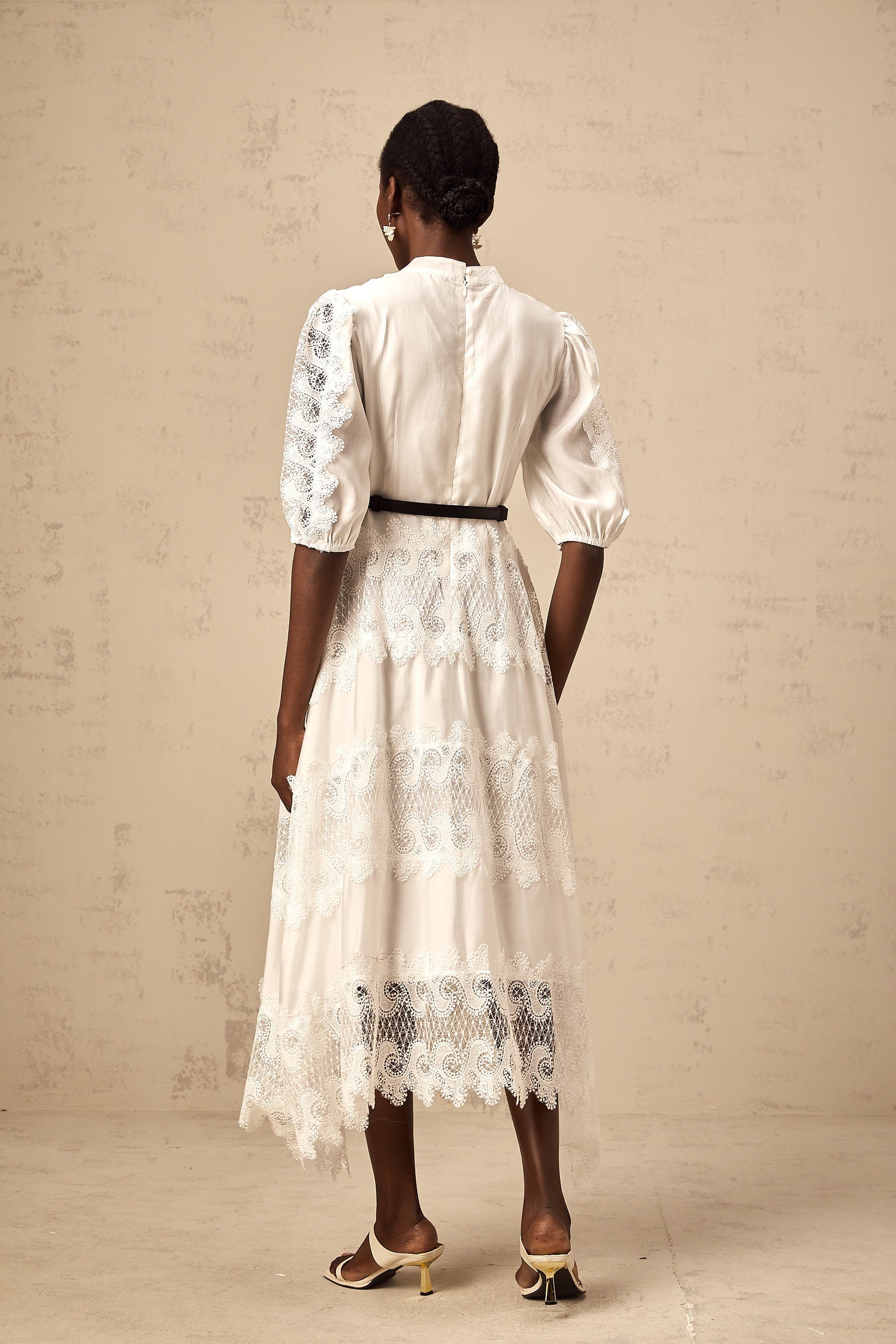 Woman wearing white midi dress with lace trim panels and belt at waist