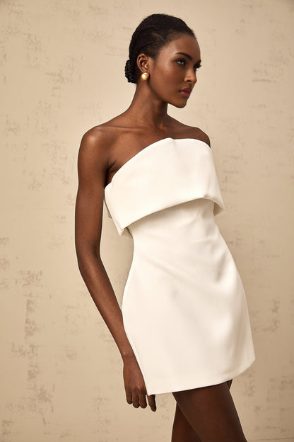 Woman wearing white off shoulder mini dress with puff sleeves standing against plain background