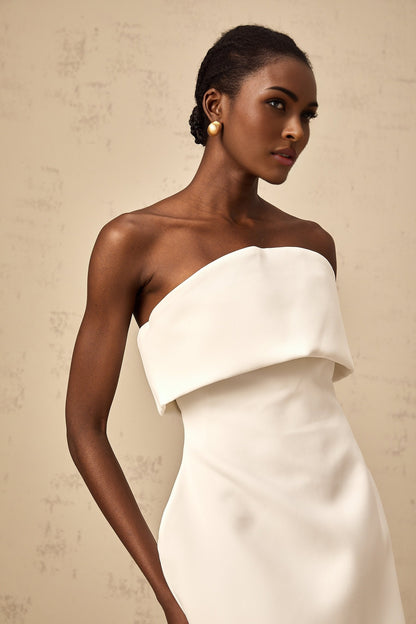 Woman wearing white offshoulder mini dress with puffed sleeves standing against plain background