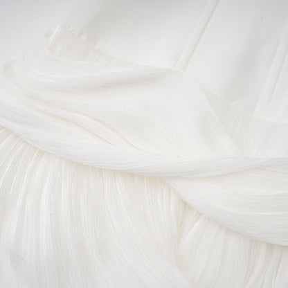 Woman wearing white pleated mini dress with cinched waist and short sleeves standing in casual pose