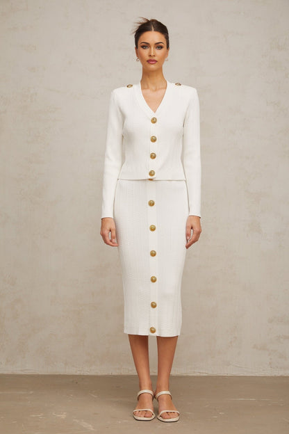 Woman wearing white ribbed knit jacket and matching skirt set standing against plain background