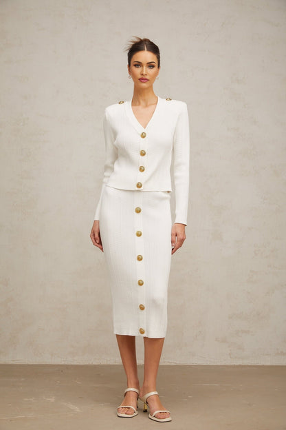 Woman wearing white ribbed knit jacket and matching skirt set standing against plain background