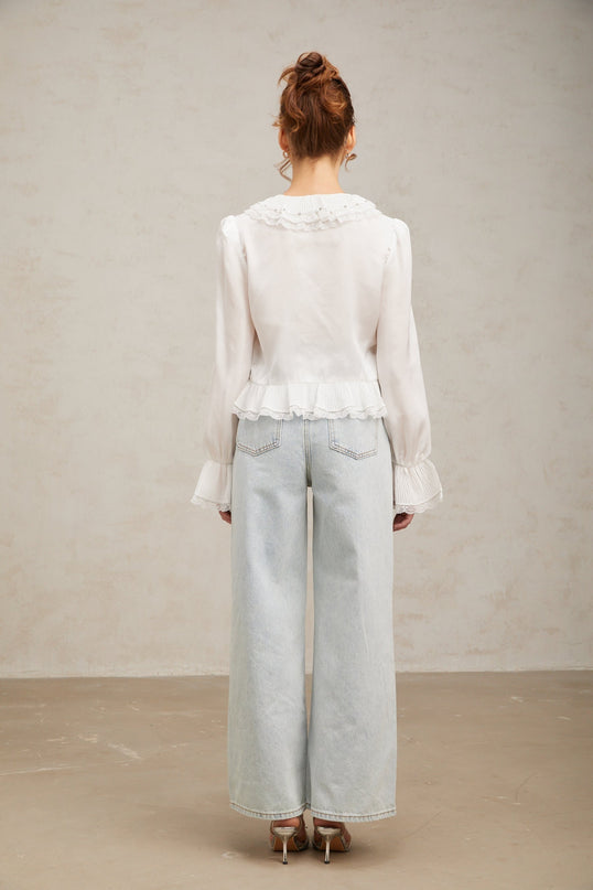Woman wearing white ruffled shirt with lace trim detail around collar and sleeves