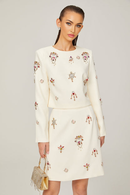 Woman wearing white twopiece outfit consisting of a crystalembellished top and matching skirt