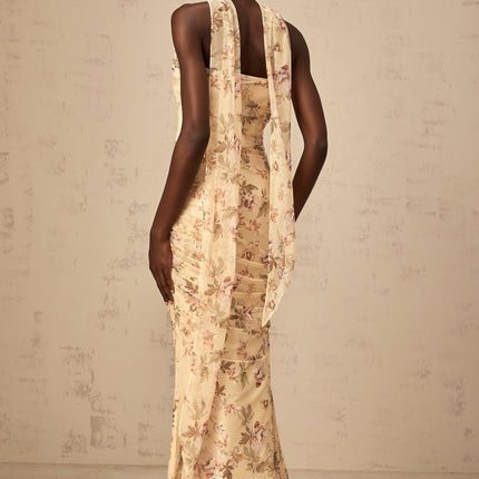 Woman wearing yellow floral print matching set with fitted top and skirt standing against white background