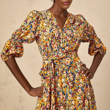Woman wearing yellow floral print midi dress with V neckline standing against plain background