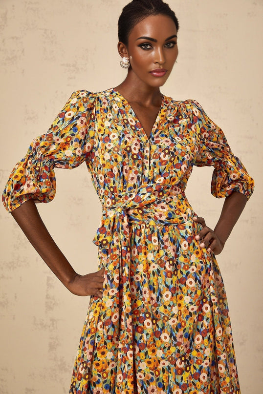 Woman wearing yellow floral print midi dress with V neckline standing against plain background
