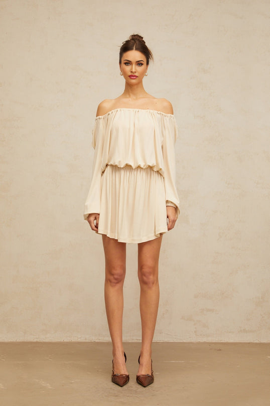 Young woman wearing a beige mini dress with structured design details standing against a plain background