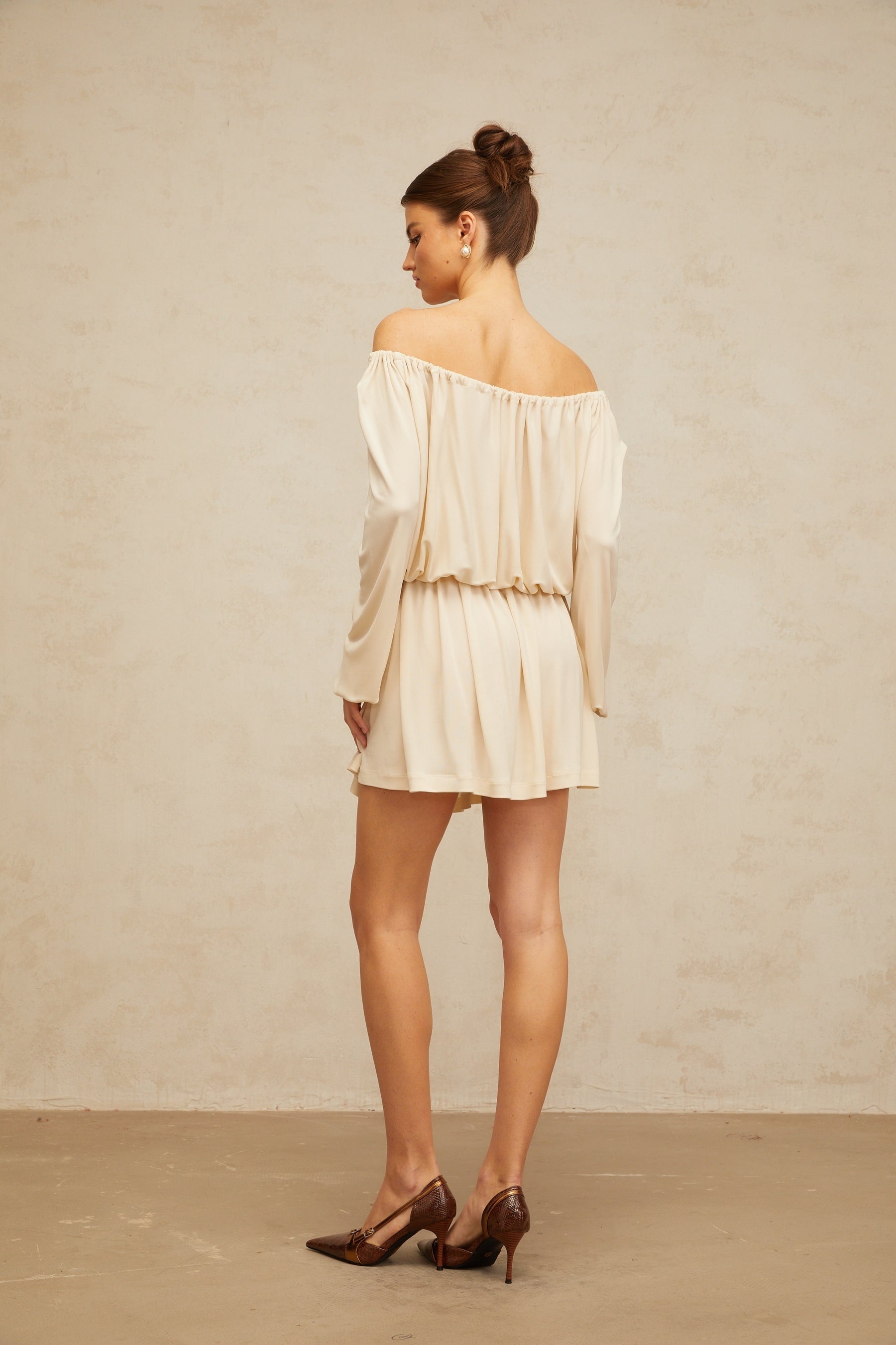 Young woman wearing a beige mini dress with structured design standing against neutral background