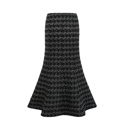 Young woman wearing a black and white checked tweed matching set consisting of a vest top and skirt standing against a plain background