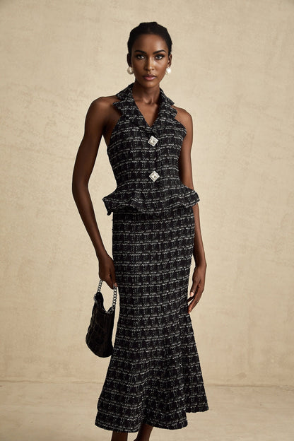 Young woman wearing a black and white checked tweed vest top and matching skirt set against a plain background