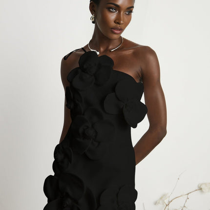 Young woman wearing a black floral offshoulder mini dress with a liane pattern standing against a plain background