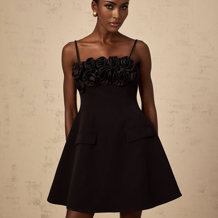 Young woman wearing a black mini dress with flared skirt and pink rose appliques walking on a white background