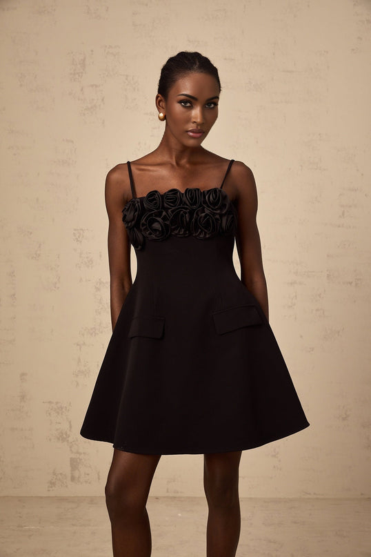 Young woman wearing a black mini dress with flared skirt and pink rose appliques walking on a white background