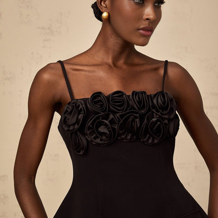 Young woman wearing a black mini dress with flared skirt and rose applique details on the bodice