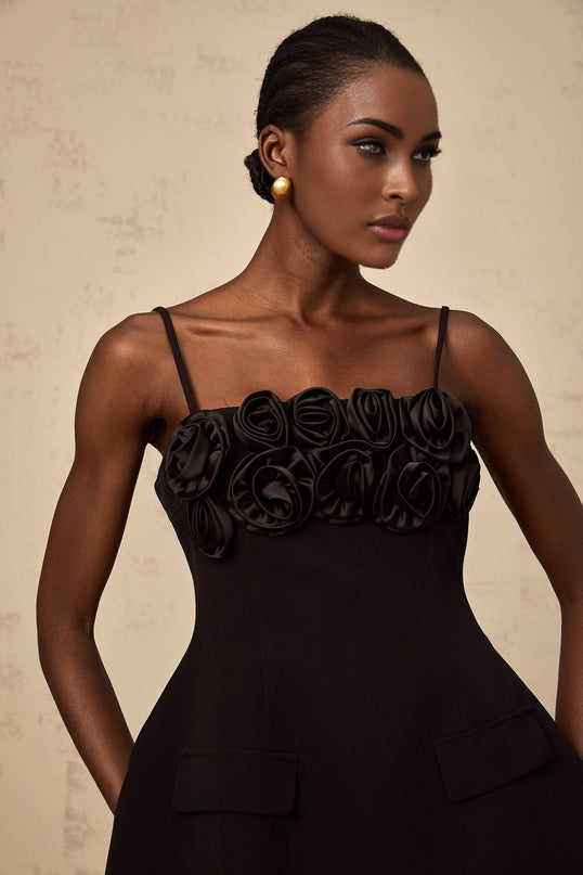Young woman wearing a black mini dress with flared skirt and rose applique details on the bodice