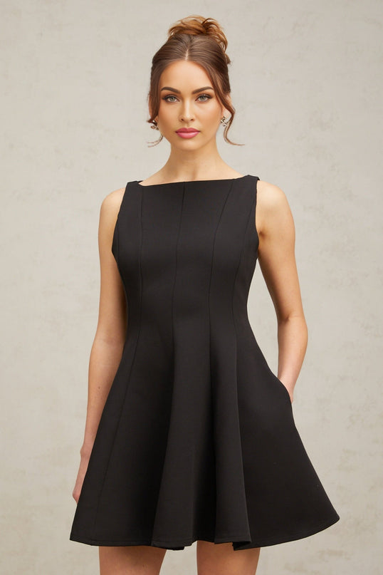 Young woman wearing a black sleeveless mini dress with a flared skirt standing against a plain background