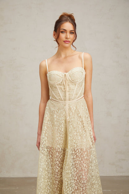 Young woman wearing a light green midi dress with floral embroidery details standing in front of a plain background