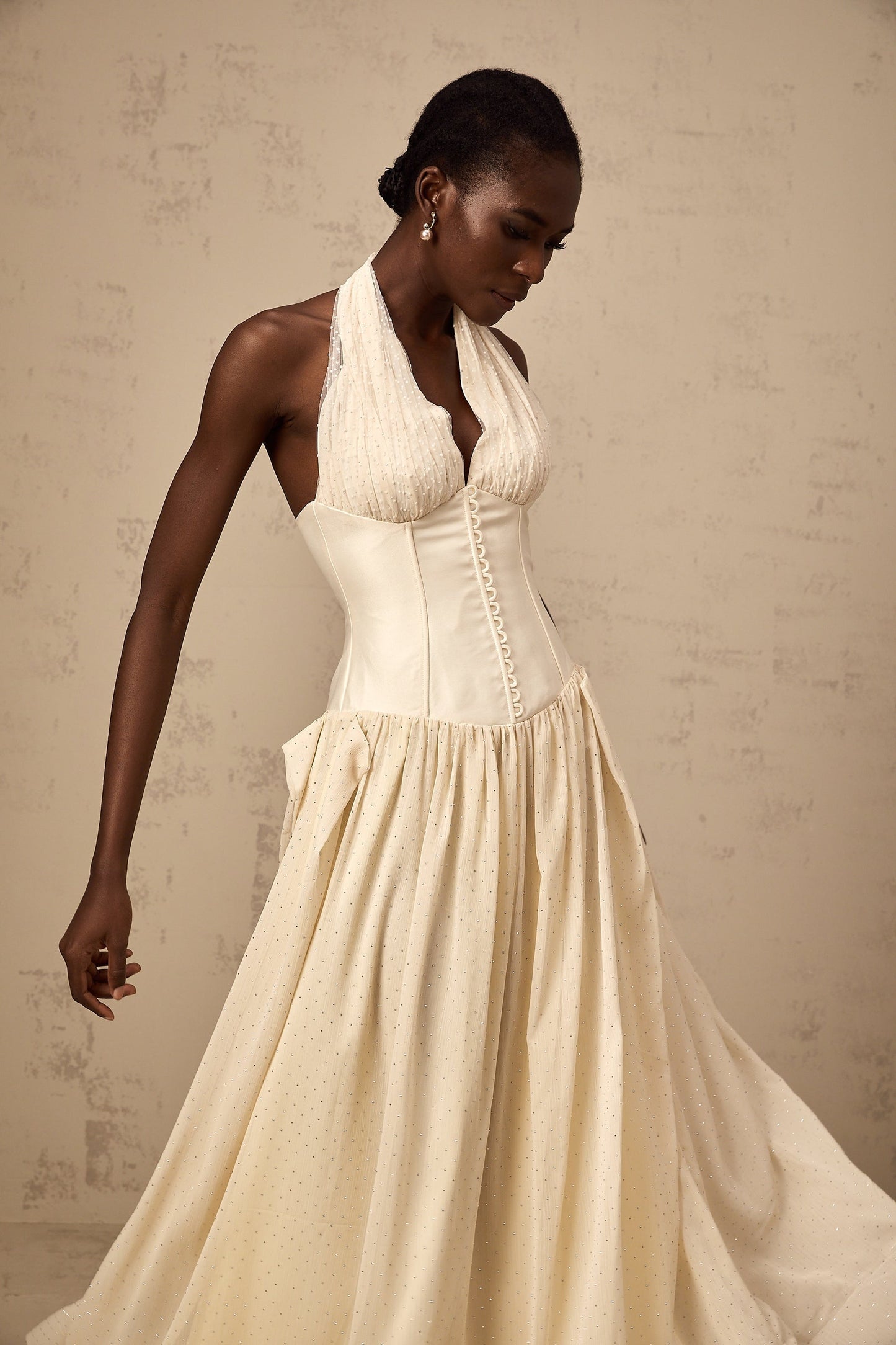 Young woman wearing a light pink halterneck tulle midi dress with a fitted bodice and flowy skirt standing in a neutral background