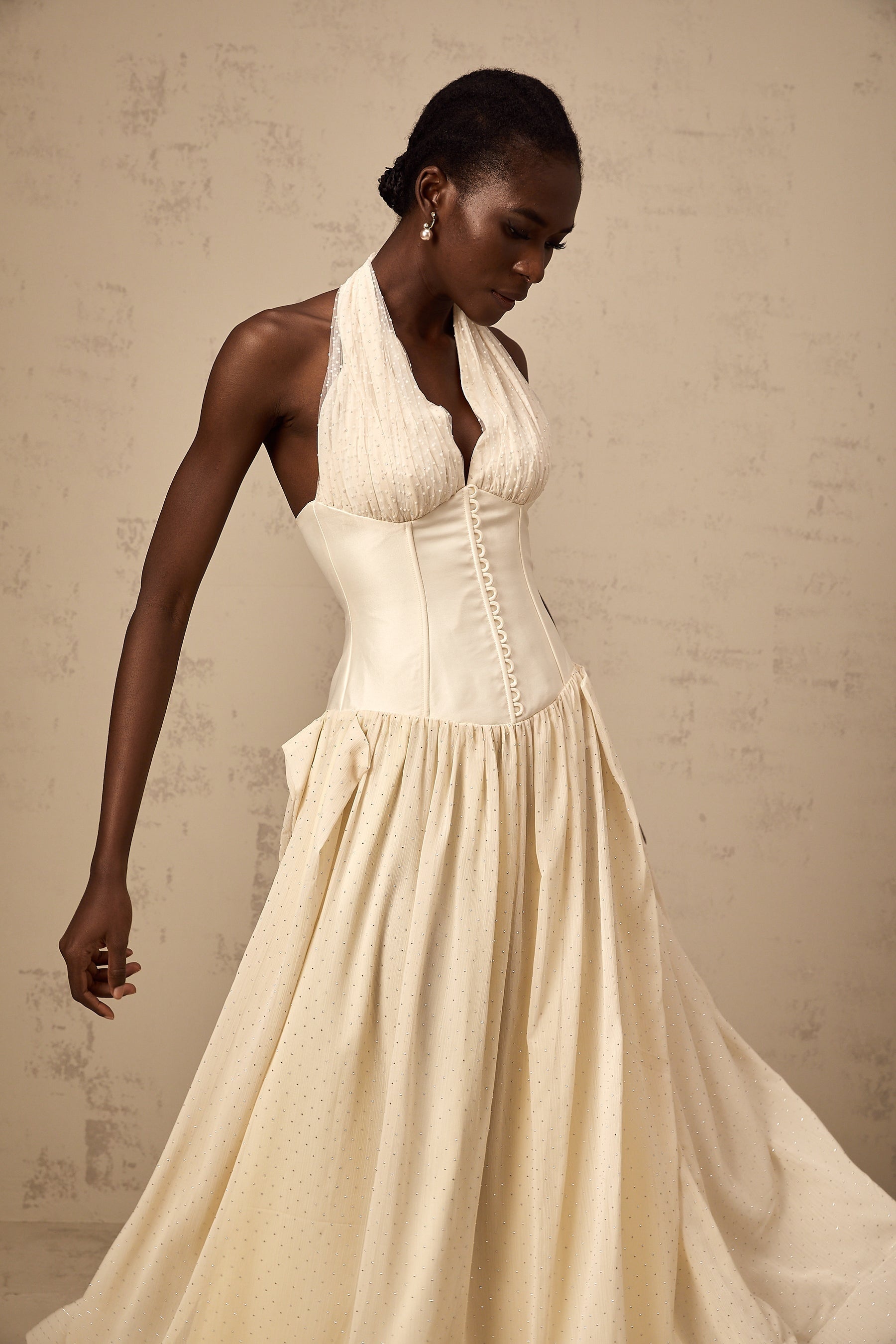 Young woman wearing a light pink halterneck tulle midi dress with a fitted bodice and flowy skirt standing in a neutral background