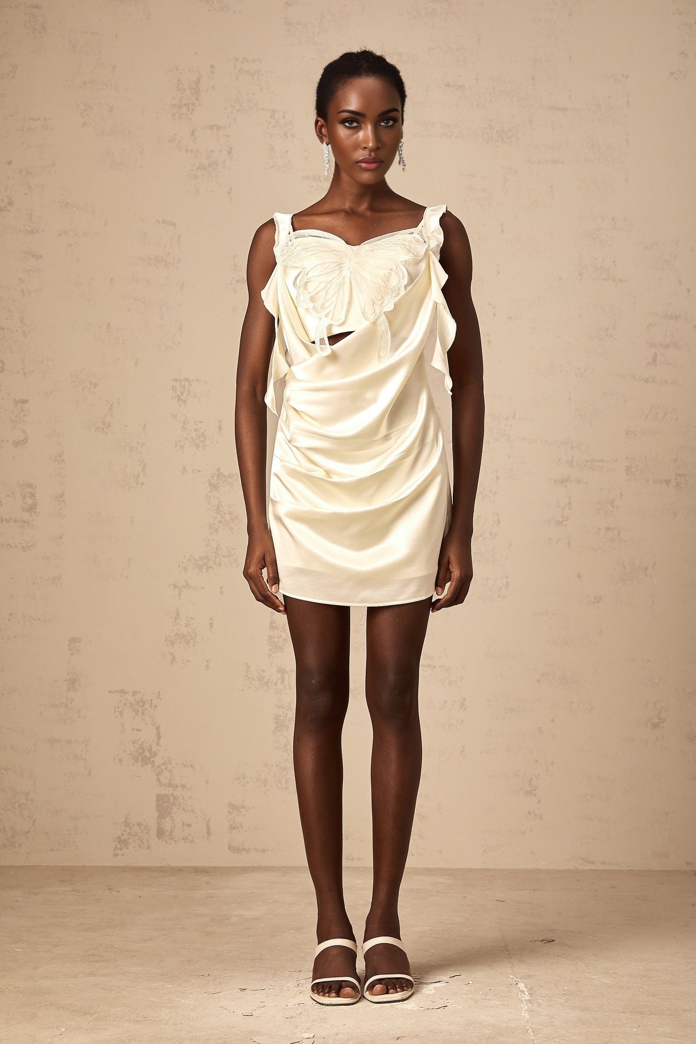 Young woman wearing a lightcolored mini dress with butterfly print and draped design standing in a neutral background