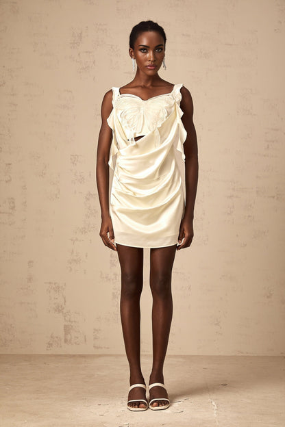 Young woman wearing a lightcolored mini dress with butterfly print and draped design standing in a neutral background