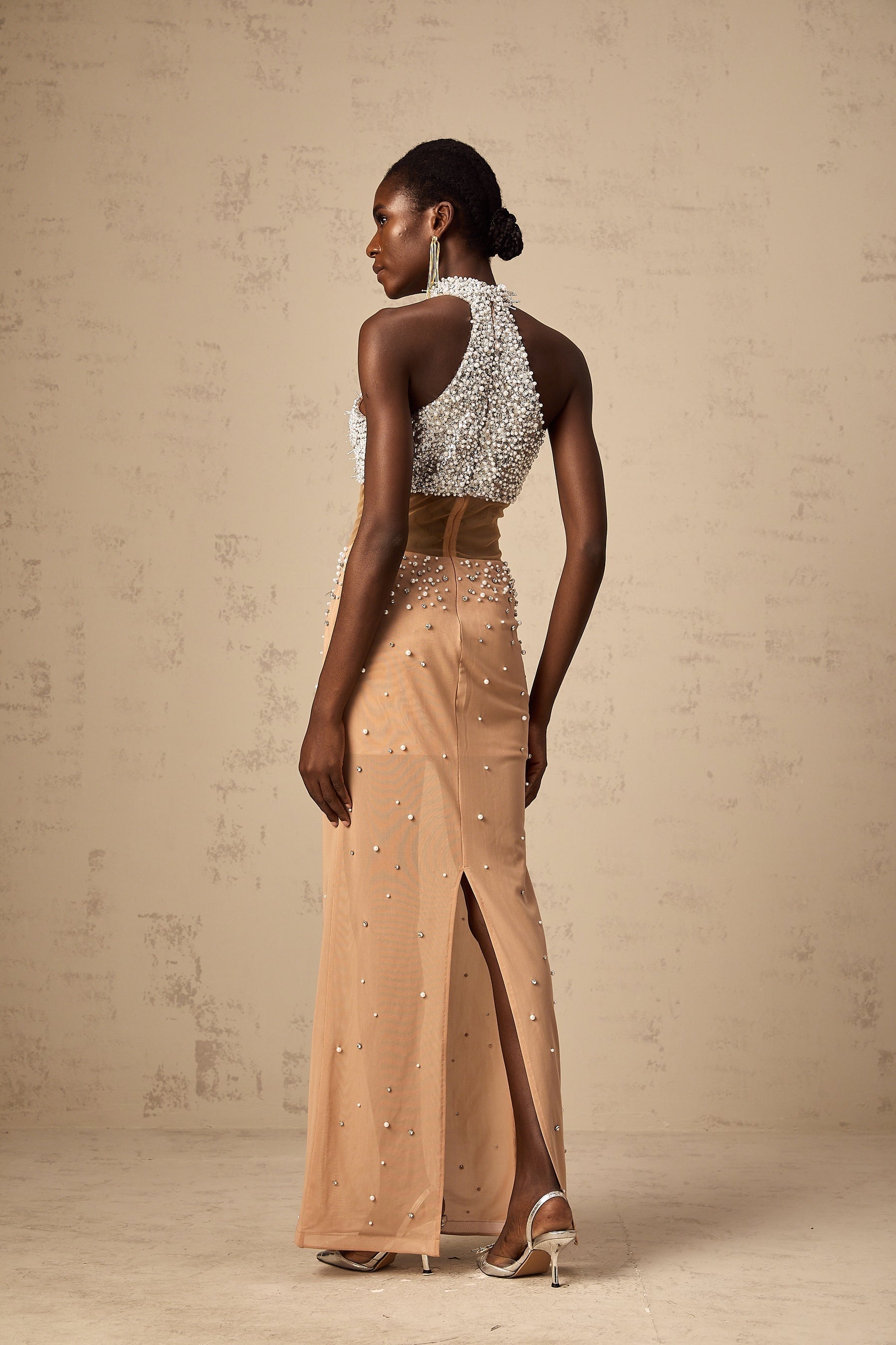 Young woman wearing a long flowy white semi sheer maxi dress with faux pearl embellishments walking on a beach